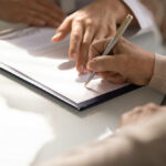 Close up of aged woman hand signing legal documents at gov office.