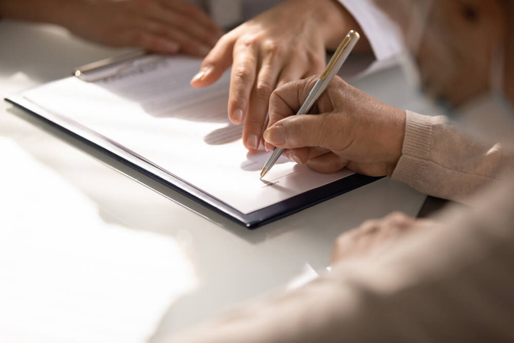 Close up of aged woman hand signing legal documents at gov office.