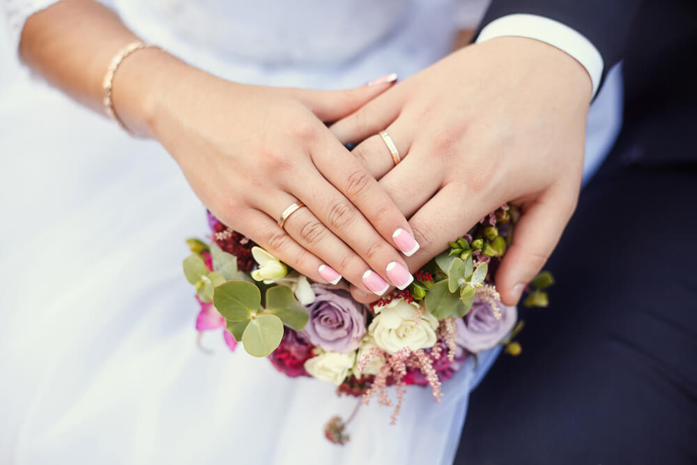 Hands of bride and groom with rings on wedding bouquet.