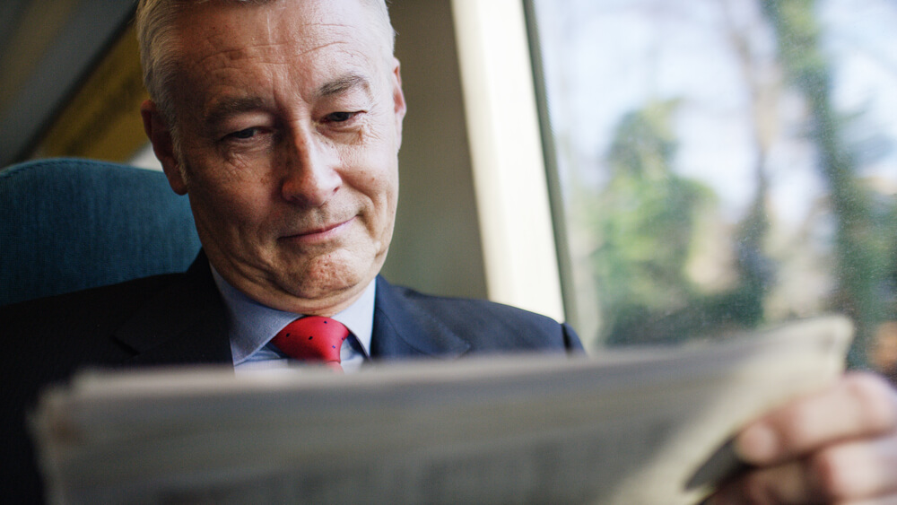 Un inversionista de negocios maduro leyendo un periódico durante un viaje en tren