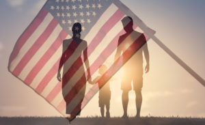Happy family walking together at sunset holding hands agains the flag of America USA background.