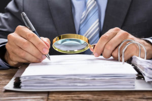 Midsection of businessman examining invoice with magnifying glass at desk