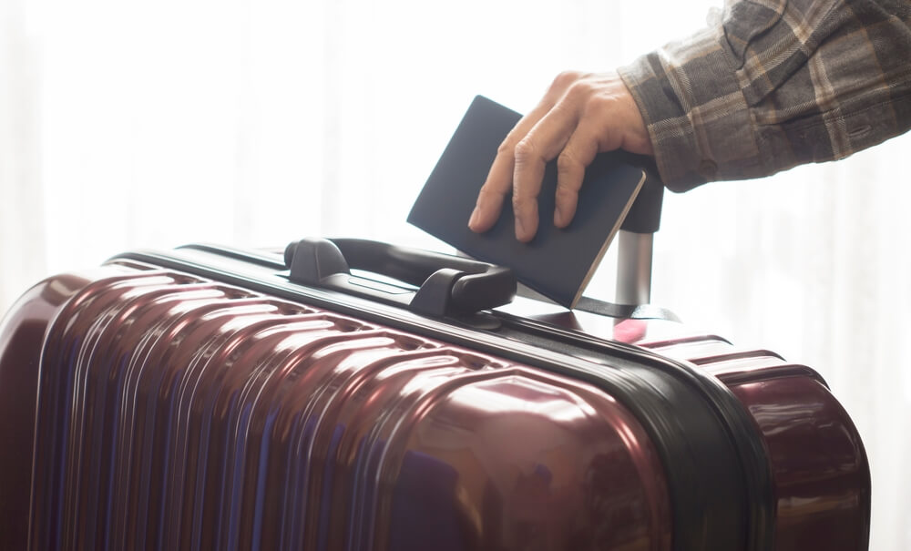 Hand holding a passport and suitcase or luggage handle.