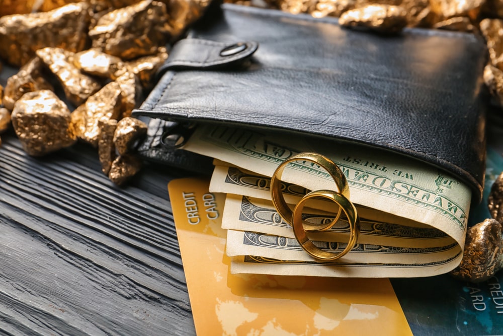 Wedding rings, wallet with money, credit cards and gold on table. Marriage of convenience